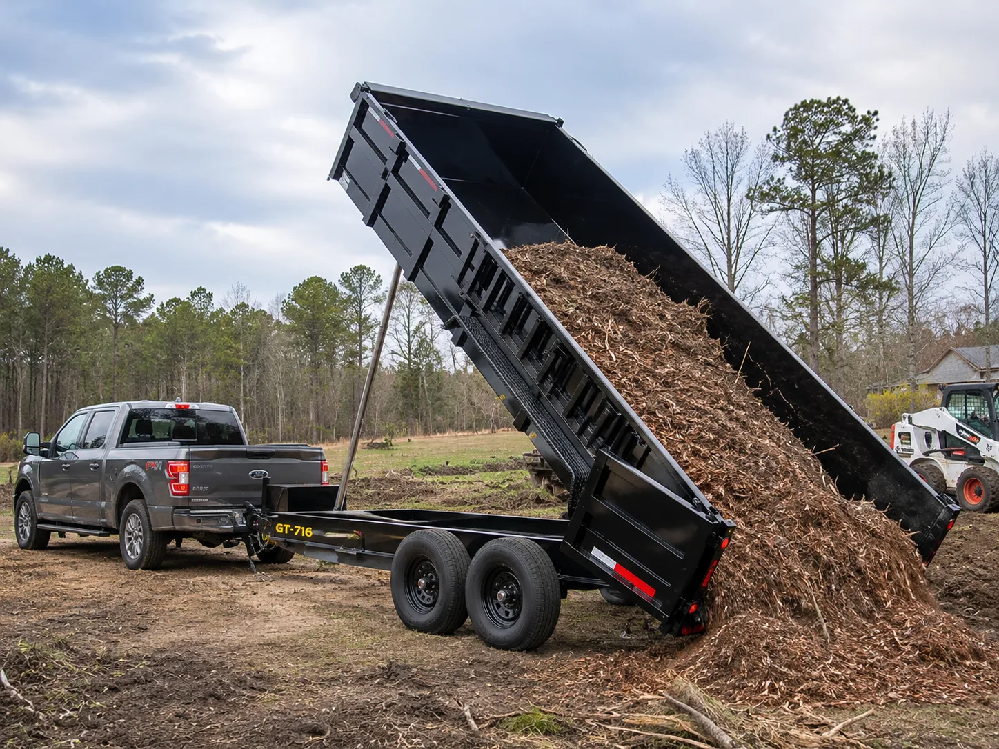 Dump trailer dumping mulch behind a pickup truck